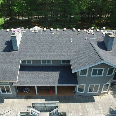 Aerial view of a gray-roofed house with two chimneys and a wooden deck, surrounded by trees.