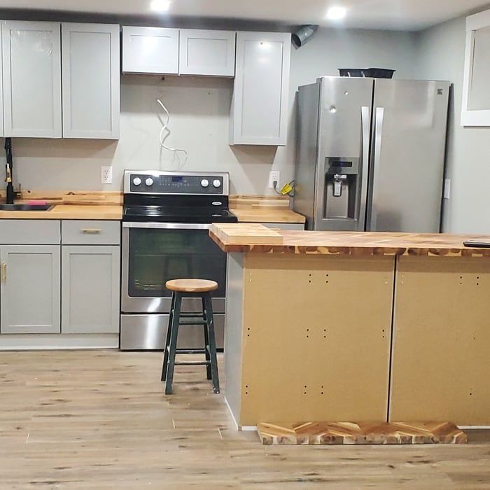 Modern kitchen with stainless steel appliances, gray cabinets, and a wooden island with a stool