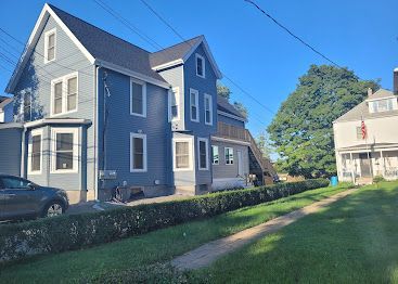 Blue house with white trim beside a grassy yard under a clear blue sky