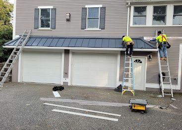 Workers on ladders installing solar panels on a gray townhouse roof above two garage doors
