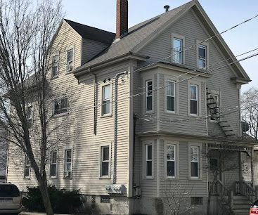 Two-story beige house with many windows and a bare tree in front