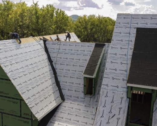 Partially shingled roof under construction with white underlayment and surrounding trees