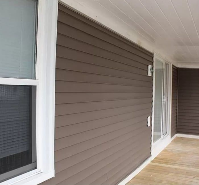 Covered porch with brown siding, white-trim windows, and a wooden floor.