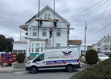 Worker on ladder repairing a white house roof, with a blue and white service van parked in front