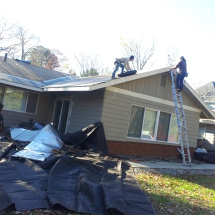Workers repairing a roof on a damaged house with a ladder and torn black tarp