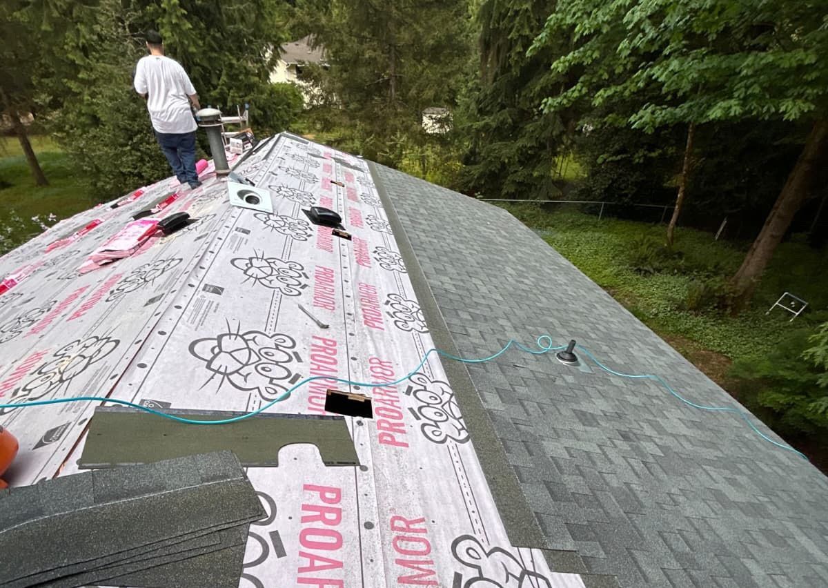 Roofers working on a house roof with pink underlayment on one side and gray shingles on the other.