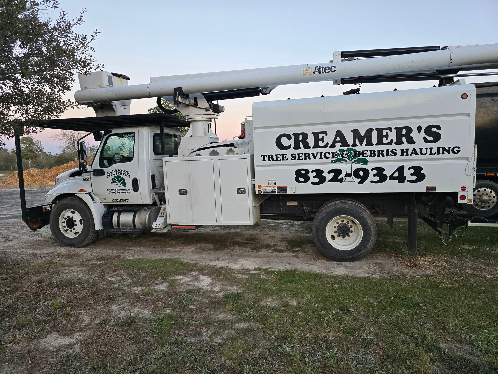 A white truck with a crane on top of it is parked in a dirt field.