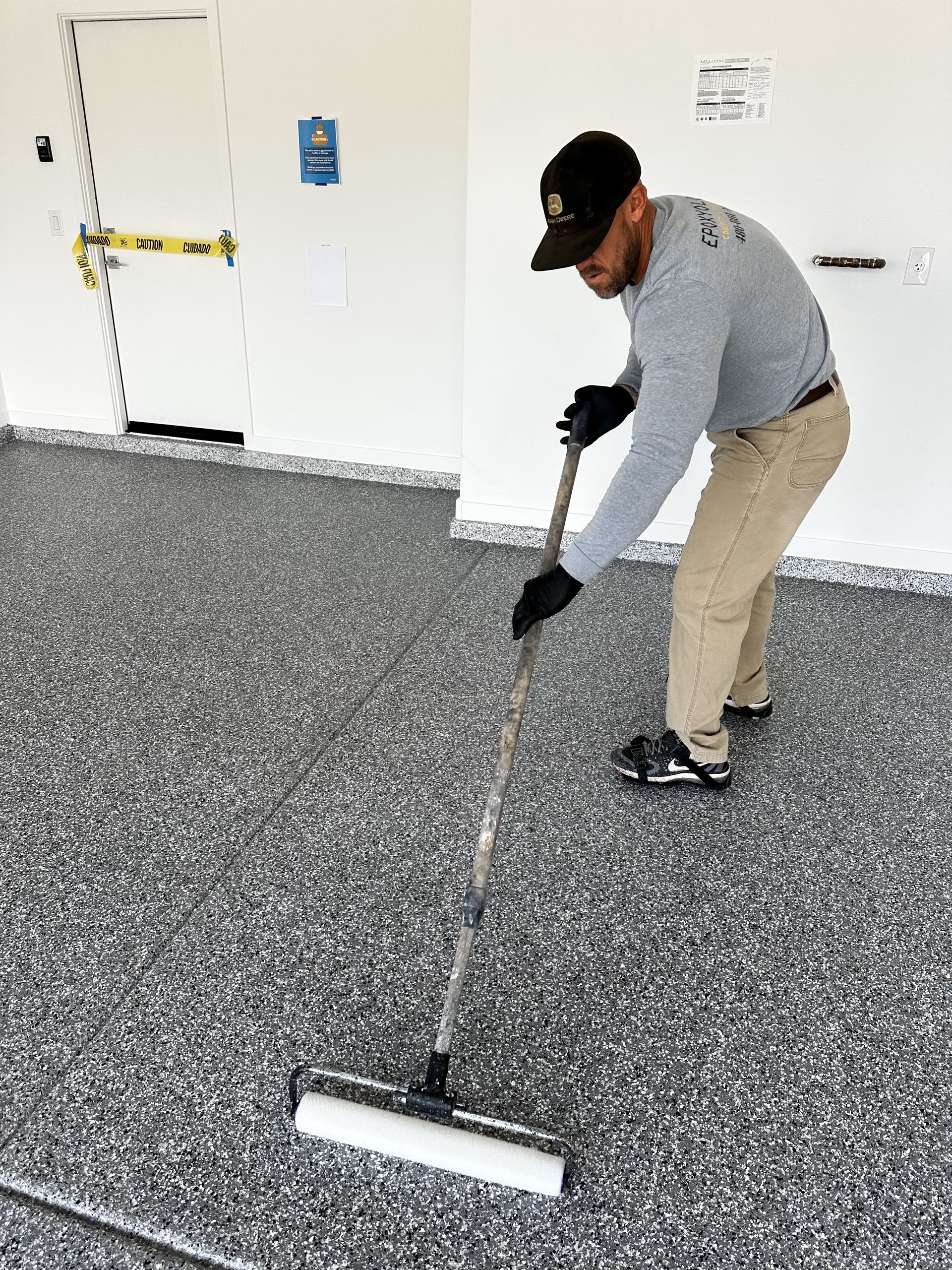 A man is painting a garage floor with a roller.