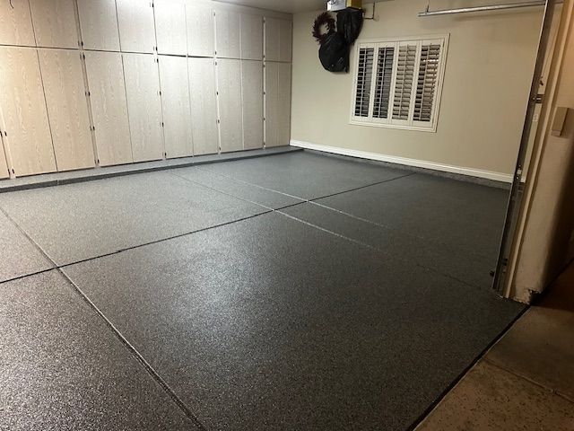 A large gray floor in a garage with lots of cabinets and a window.