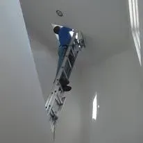 Person on a ladder reaching into a hole in the ceiling, angled shot.