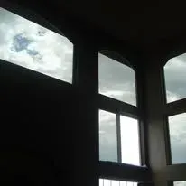 Inside view of tall windows, cloudy sky visible, dark interior.