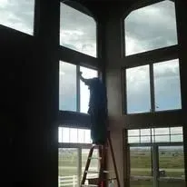 Person on a ladder, cleaning large windows in a tall, multi-paned structure.
