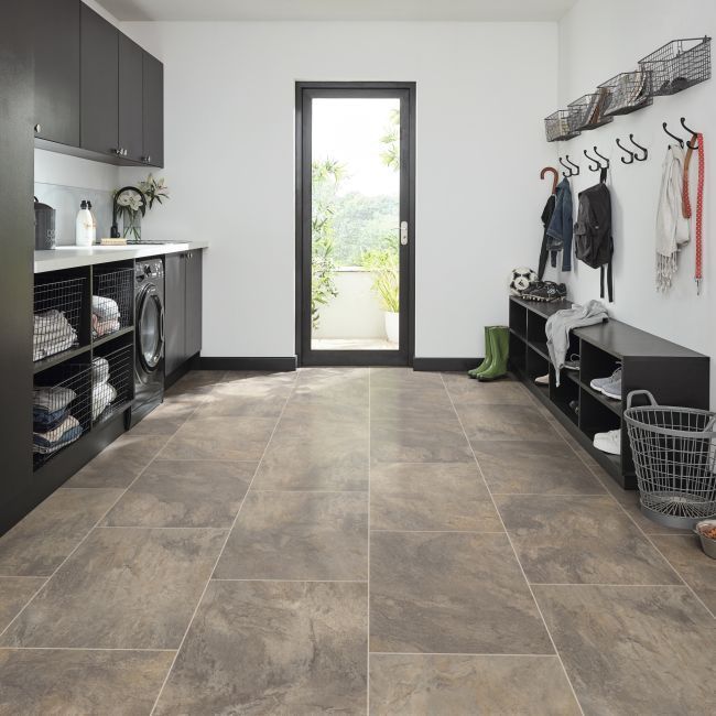 Laundry room with dark cabinets, washer, shelving, open door, and tiled floor.