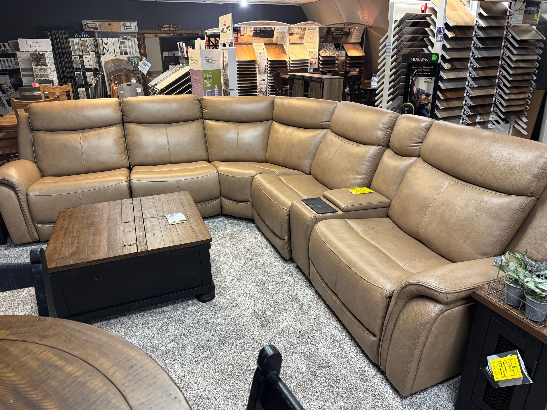 Tan leather sectional sofa in furniture store. Includes a wooden coffee table and side table.