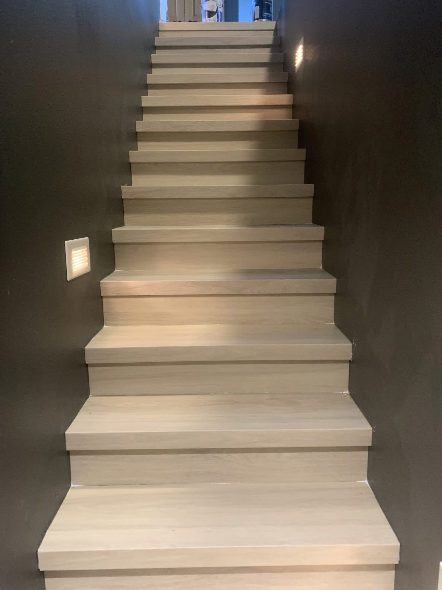 Wooden staircase with light steps and dark walls, ascending upwards.