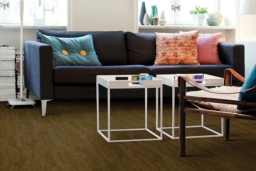 Living room with dark sofa, white tables, and patterned pillows on brown carpet.