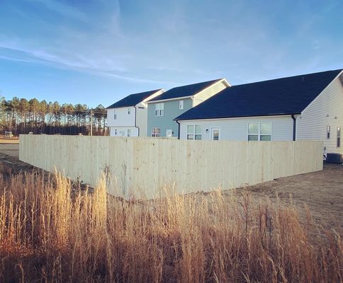 A wooden fence is surrounded by tall grass in front of a house.