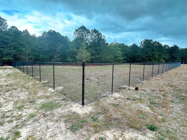 A chain link fence surrounds a field with trees in the background.