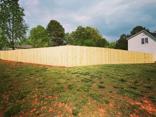 A wooden fence surrounds a lush green field in front of a house.