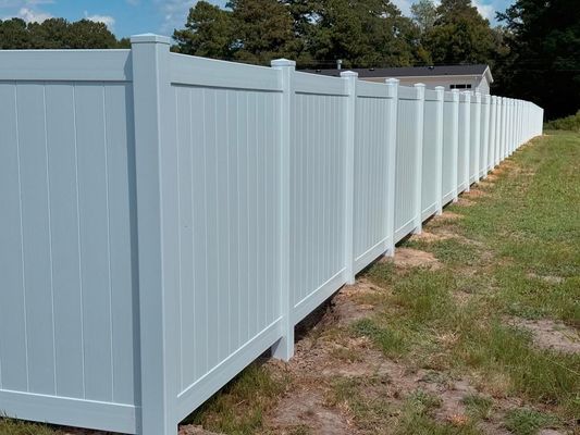 A white vinyl fence is sitting in the middle of a grassy field.