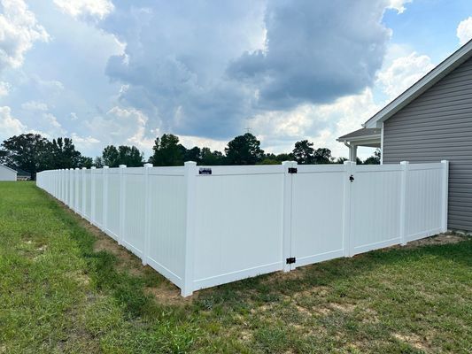 A white vinyl fence with a gate is in the backyard of a house.