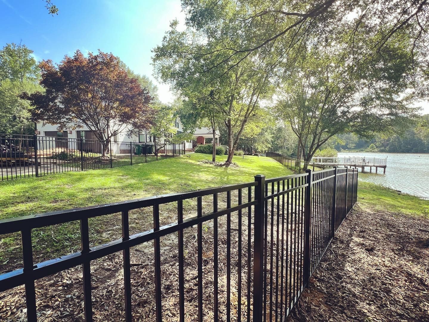A black fence surrounds a grassy area next to a lake.