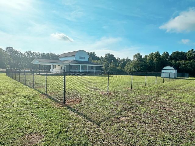 A large grassy field with a fence around it and a house in the background.