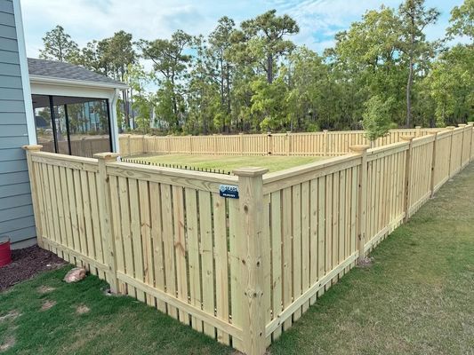 A wooden fence surrounds a lush green yard in front of a house.