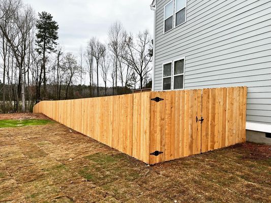 A wooden fence is surrounding a house in a backyard.