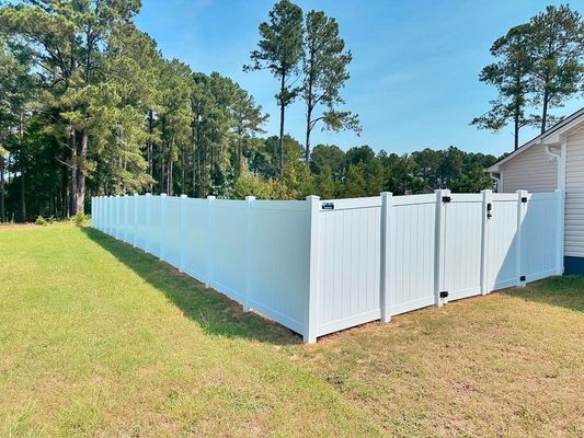 A white vinyl fence with a gate in the backyard of a house.