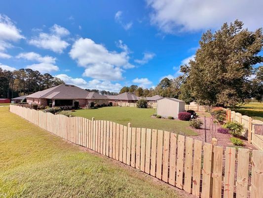 A wooden fence surrounds a lush green yard in front of a house.