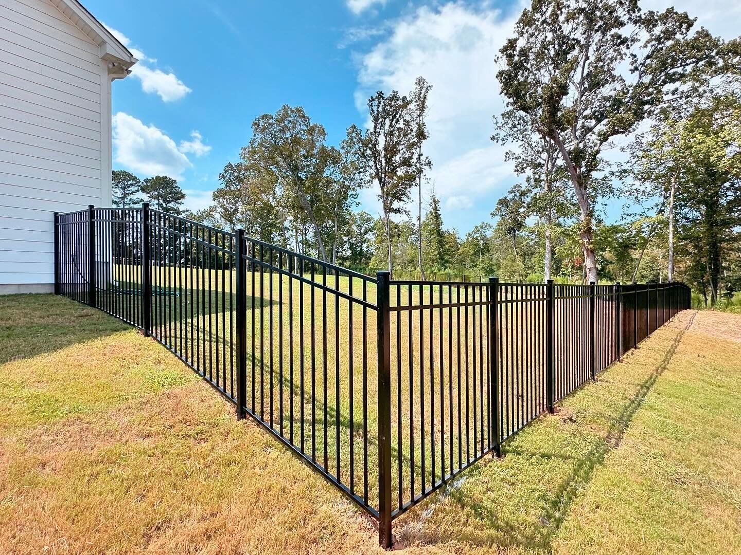 A black metal fence surrounds a grassy field in front of a house.