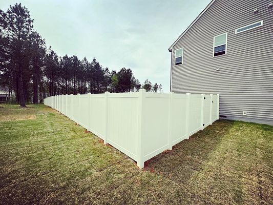 A white vinyl fence is in the backyard of a house.