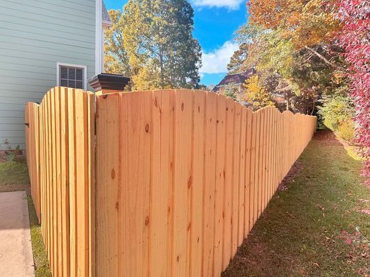 A wooden fence is surrounded by trees and grass in front of a house.
