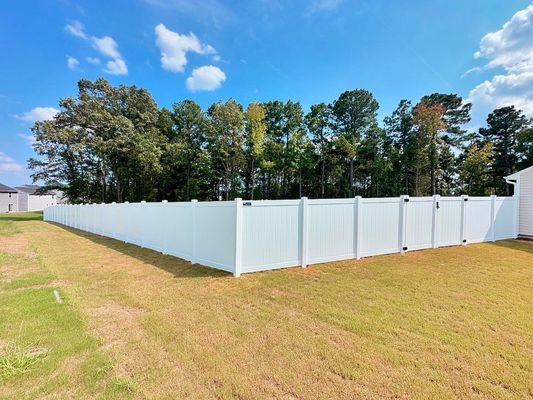 A long white fence surrounds a grassy yard with trees in the background.