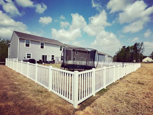 A white fence surrounds a backyard of a house.