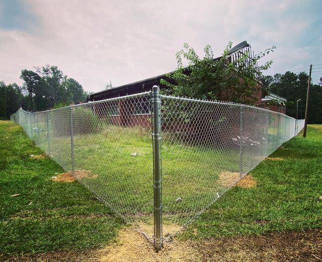 A chain link fence is surrounding a house in a grassy field.