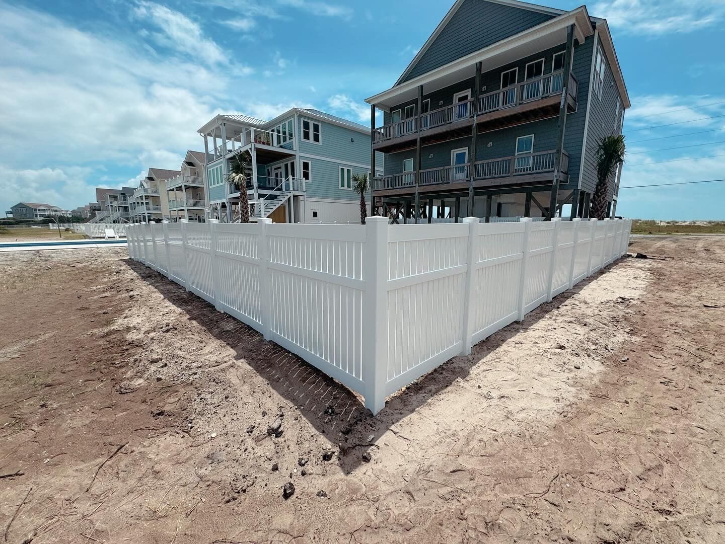 A white fence is surrounding a house on the beach.