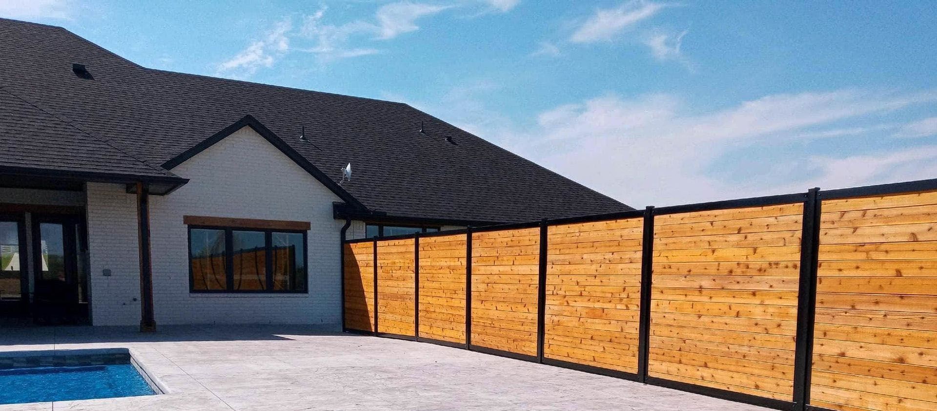 A wooden fence surrounds a swimming pool in front of a house.