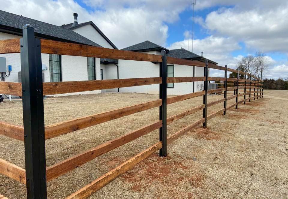 A wooden fence with black posts is in front of a house.