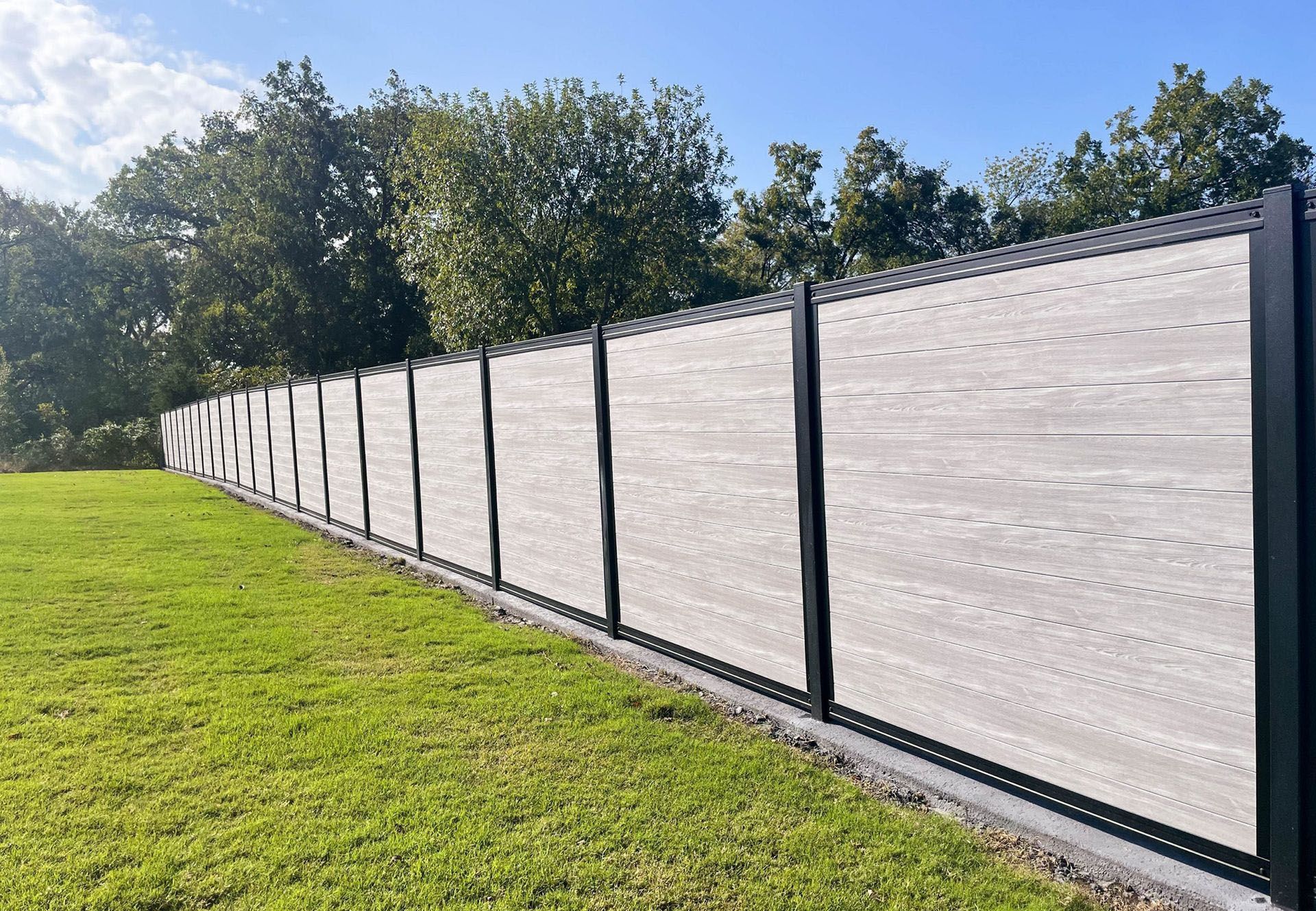 A wooden fence surrounds a grassy field with trees in the background.