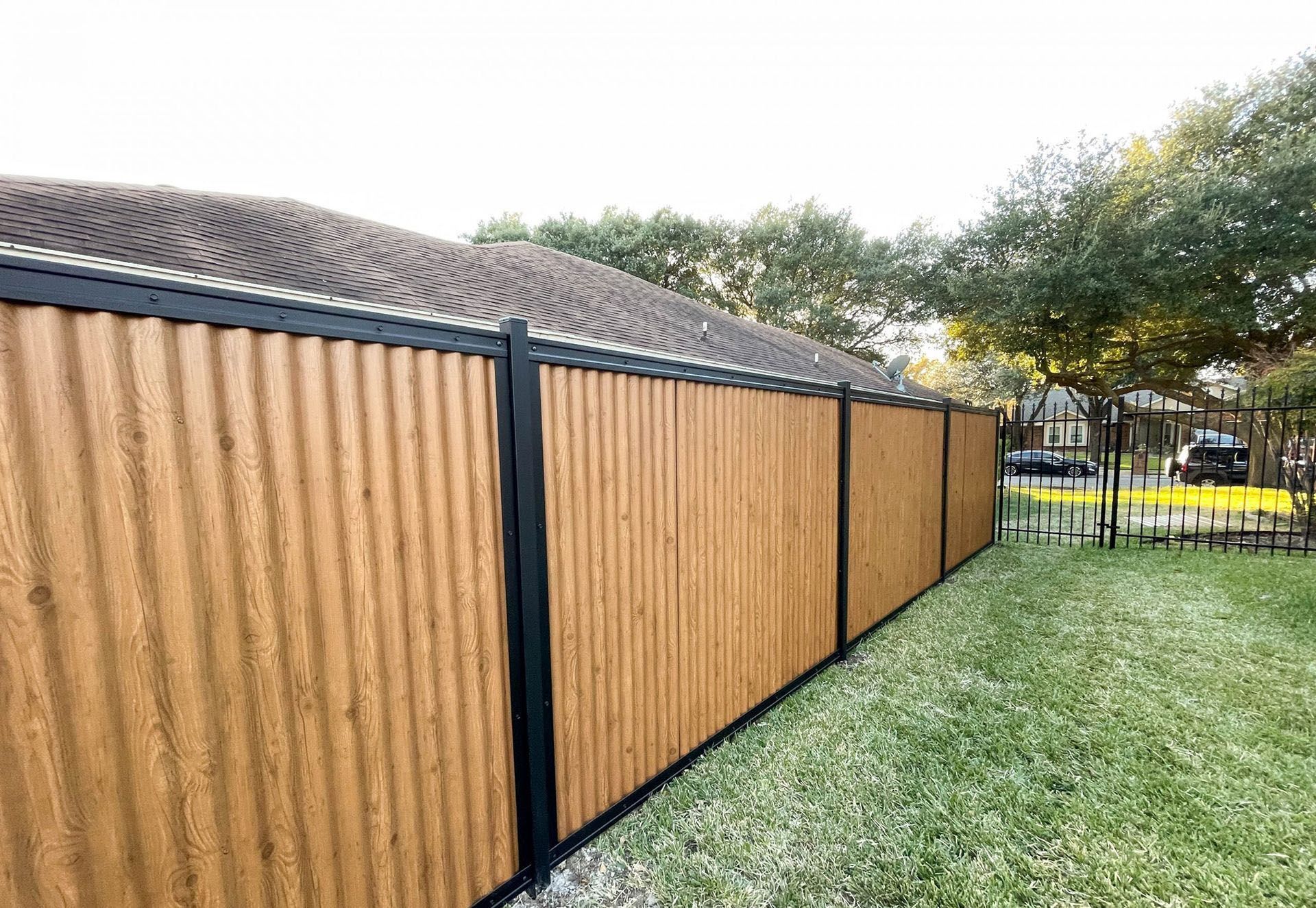 A wooden fence with a black trim is in the backyard of a house.