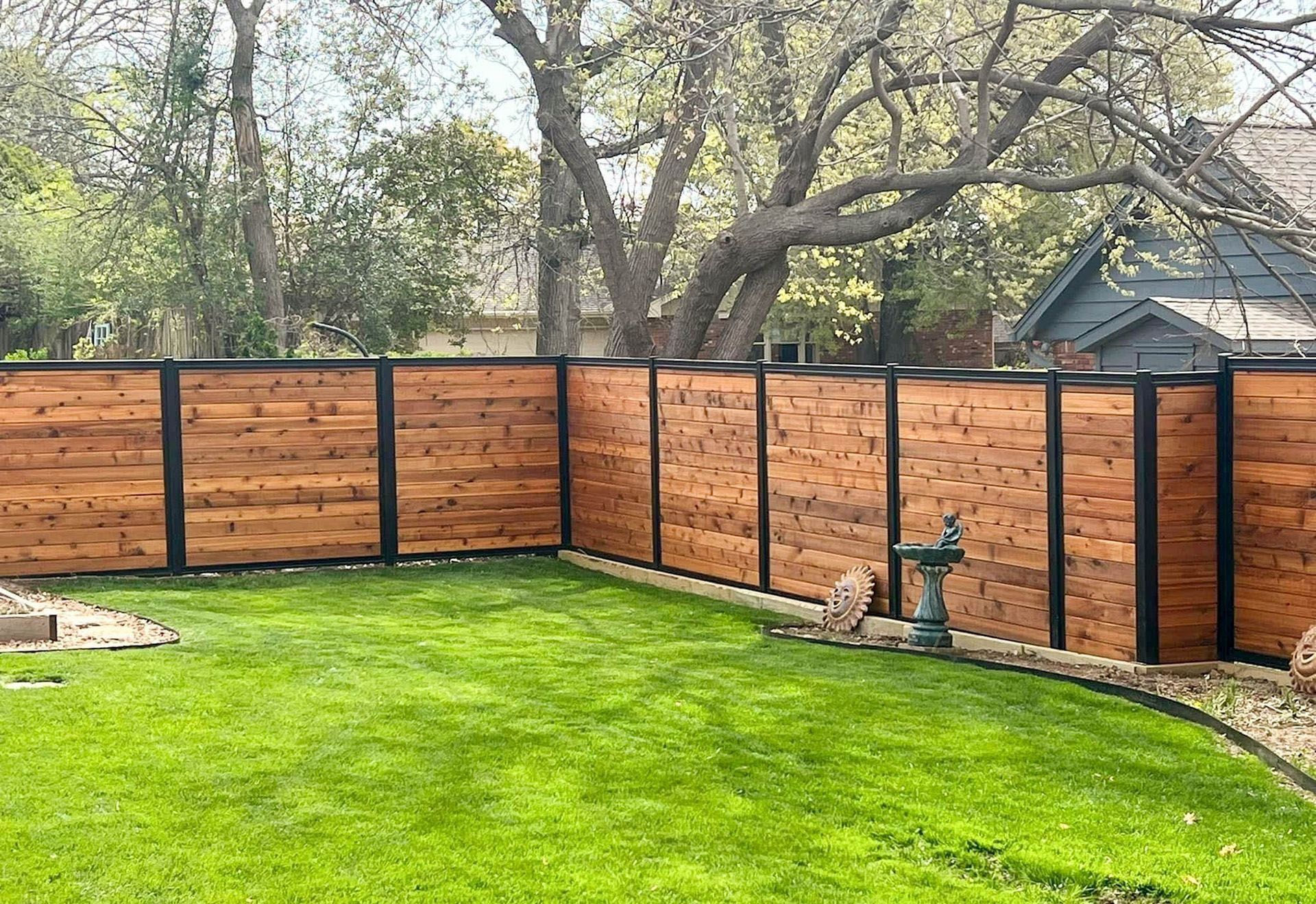 A wooden fence surrounds a lush green lawn in a backyard.