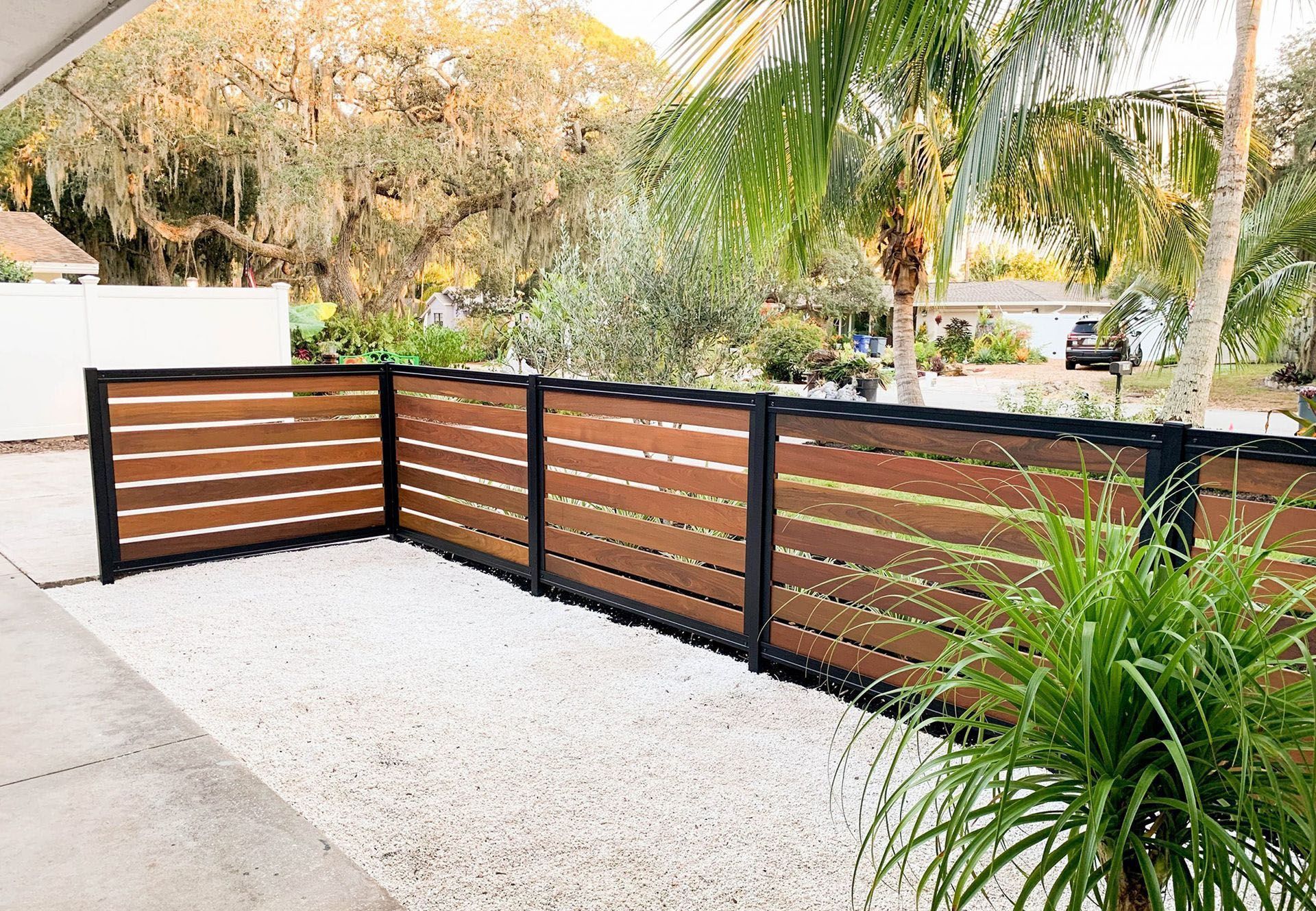 A wooden fence is surrounded by gravel and palm trees.