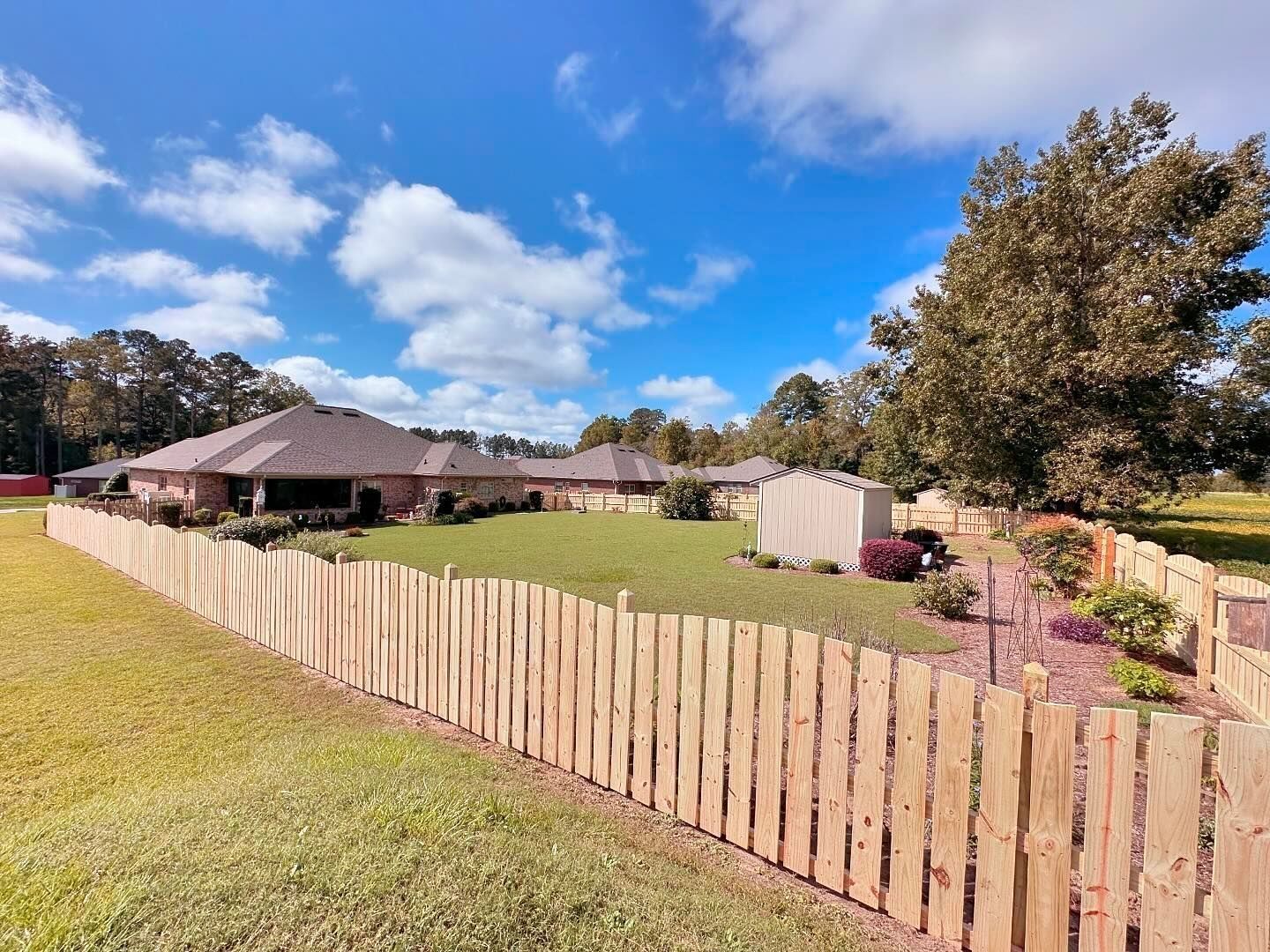 A wooden fence surrounds a lush green yard in front of a house.