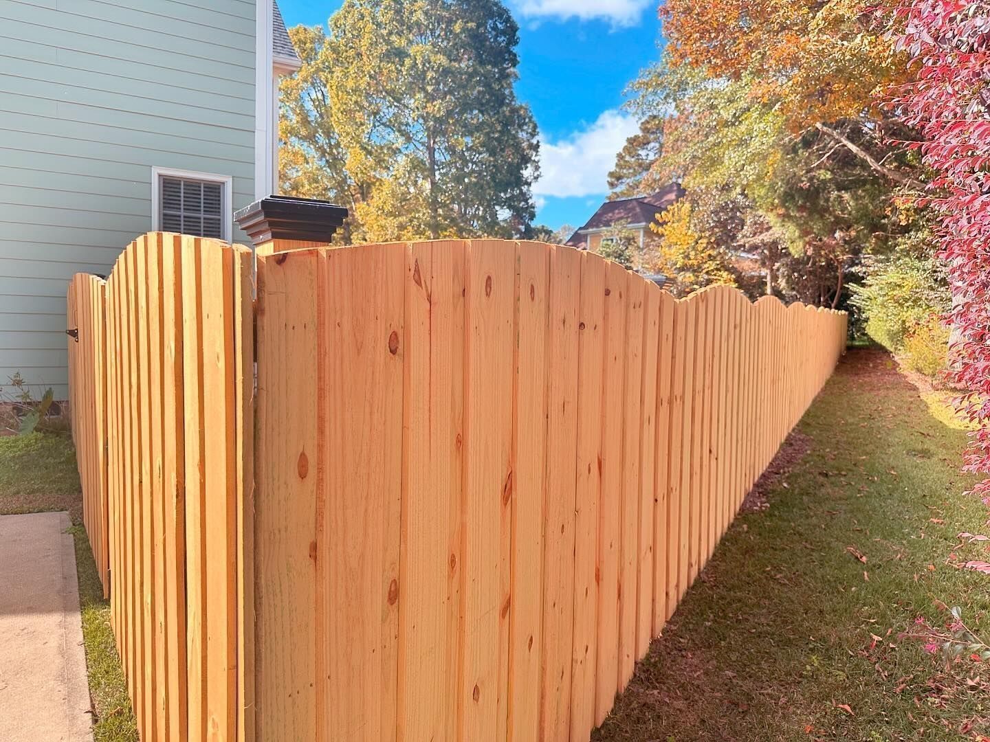A wooden fence is surrounded by trees and grass in front of a house.