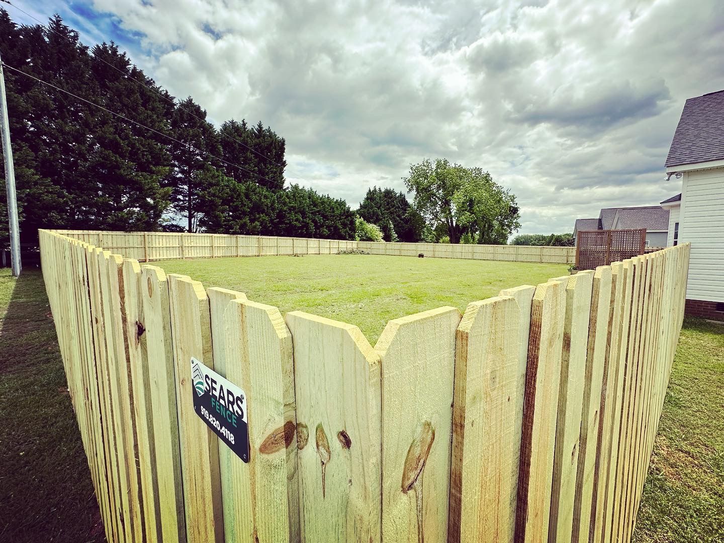 A wooden fence surrounds a grassy field in front of a house.