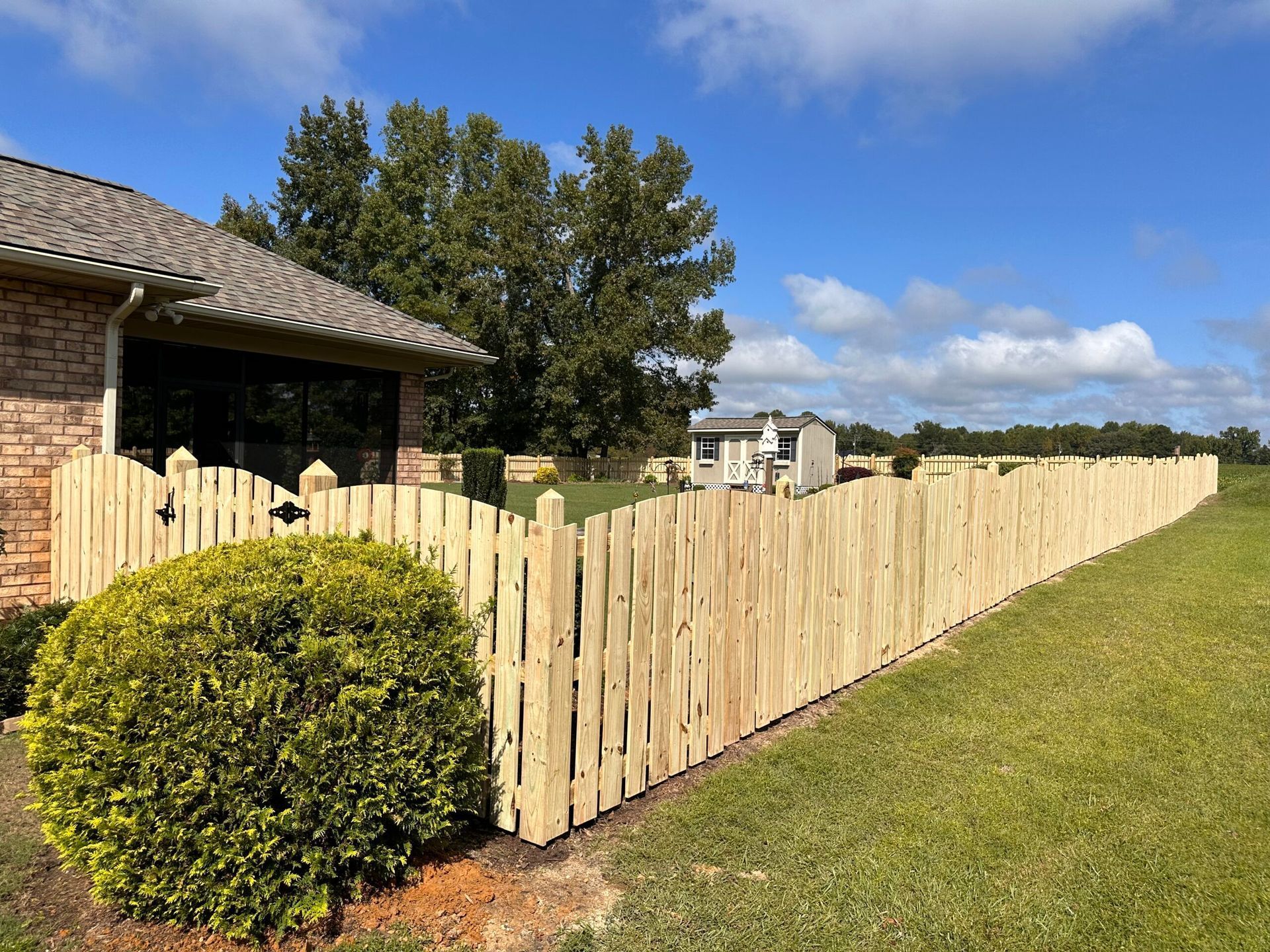 A wooden picket fence is in front of a brick house.