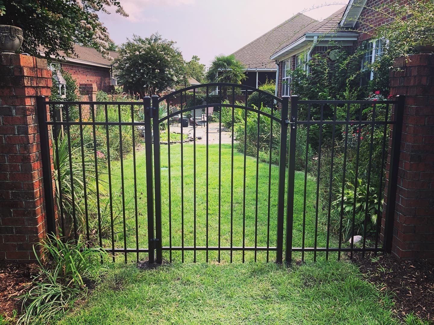 A wrought iron gate leading to a lush green yard