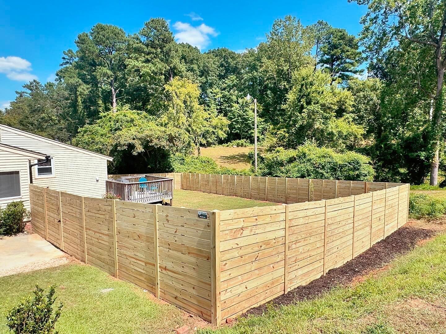 A wooden fence surrounds a lush green yard in front of a house.